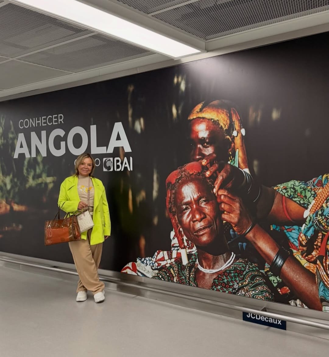 Sandra Martins ao lado de um mural 'Conhecer Angola' em um aeroporto